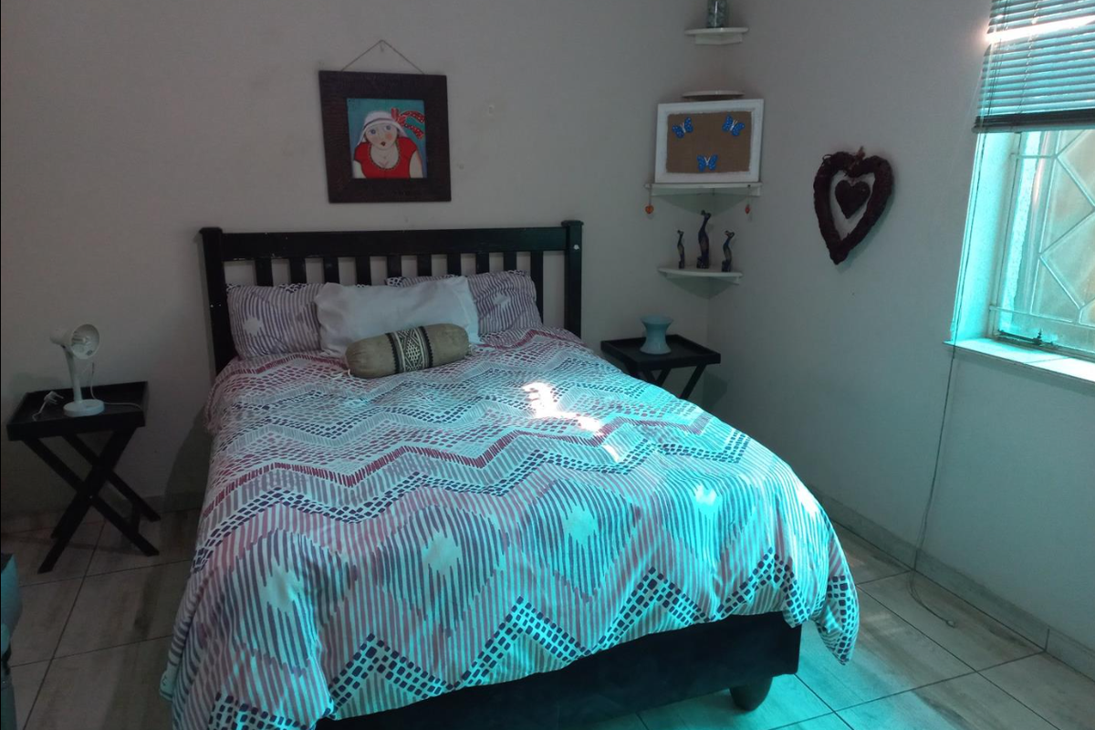 A bedroom featuring tiled flooring, corner shelving, and a window fitted with blinds and security bars.
