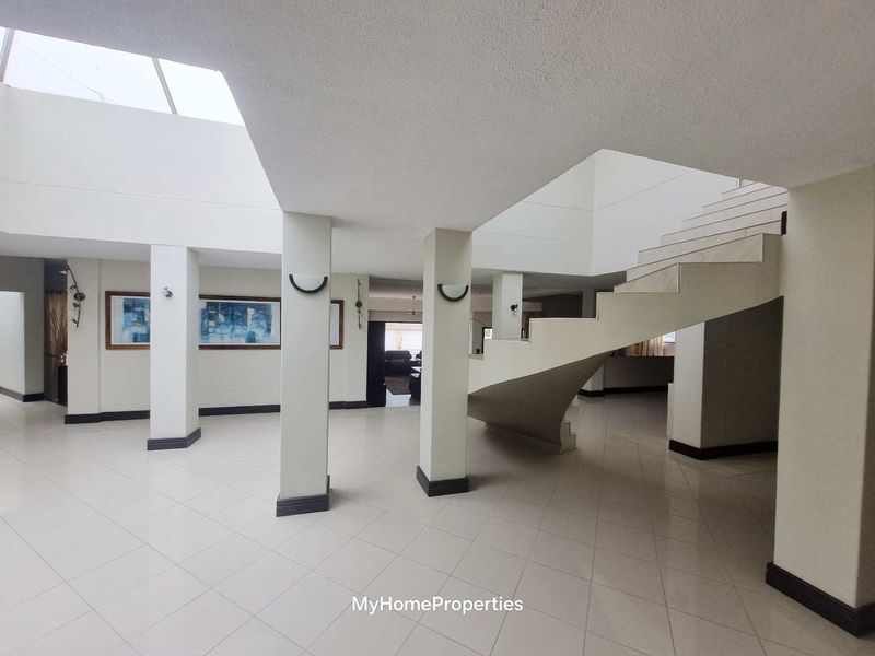 Spacious entrance hall featuring a grand staircase, tiled flooring, and a large skylight that provides ample natural light throughout the open-plan area.