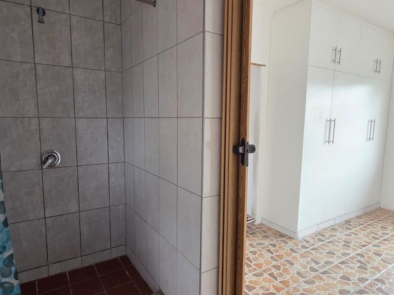 A bathroom featuring a tiled shower area adjacent to a room with built-in storage cupboards and tiled flooring.