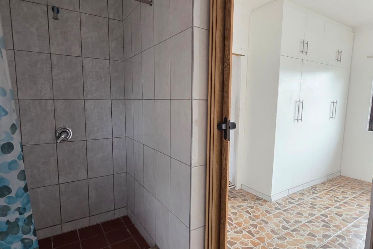 A bathroom featuring a tiled shower area adjacent to a room with built-in storage cupboards and tiled flooring.