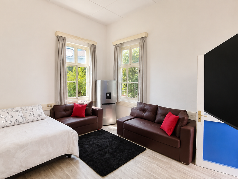 A bedroom featuring light-toned laminate flooring and dual timber-framed windows that provide natural light and garden views.