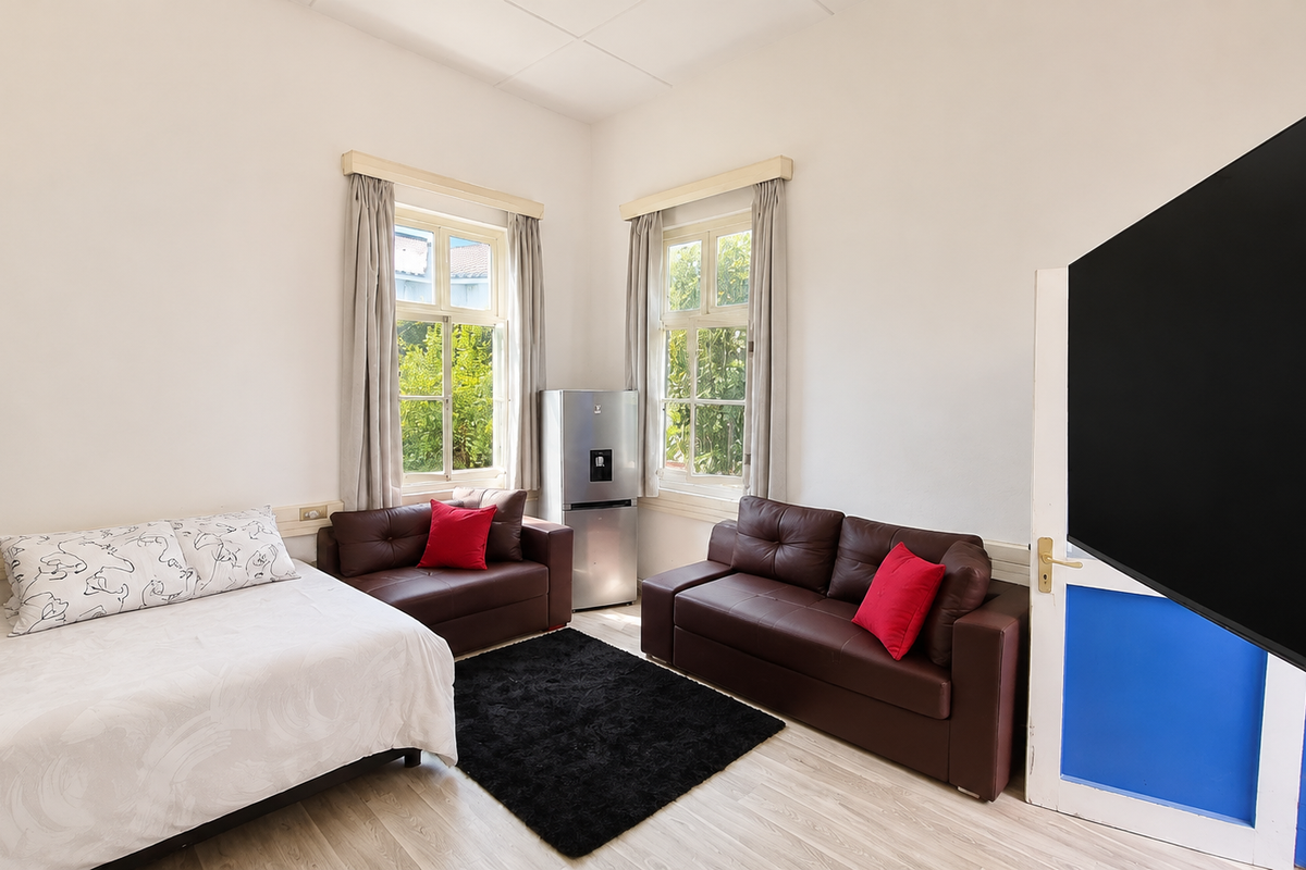 A bedroom featuring light-toned laminate flooring and dual timber-framed windows that provide natural light and garden views.