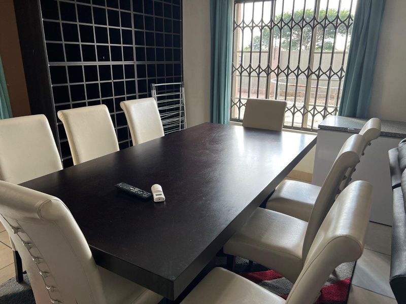 A dining area featuring a built-in dark shelving unit and a window secured with metal security bars.