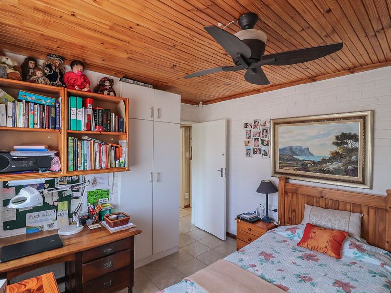 A bedroom featuring a timber tongue and groove ceiling, ceiling fan, built-in cupboards, and tiled flooring with painted brick walls.