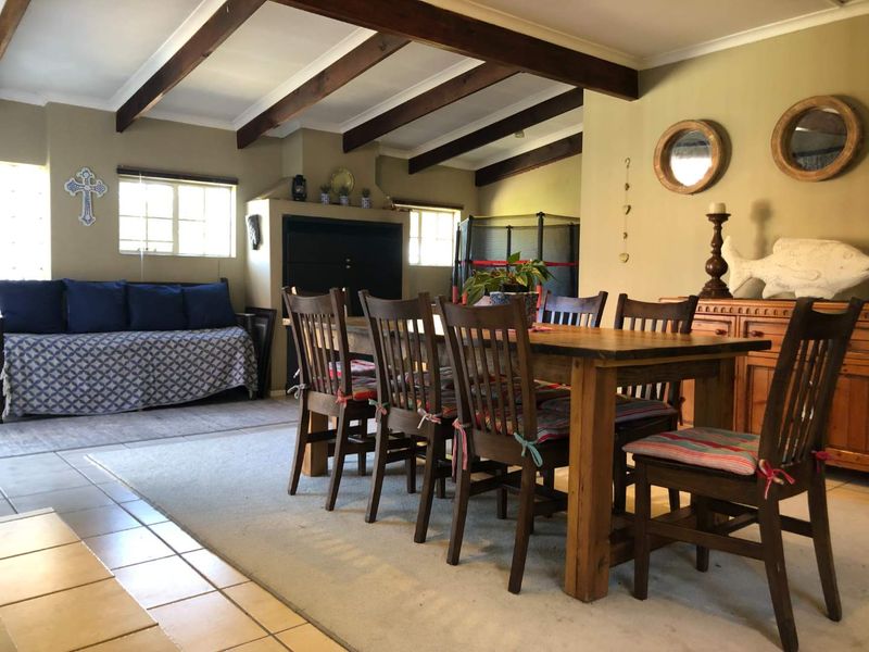 Spacious open-plan living and dining area featuring exposed timber ceiling beams, tiled flooring, and a built-in fireplace, offering a warm and rustic atmosphere.