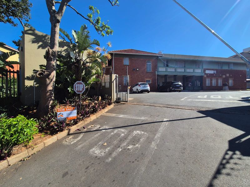 Front exterior view of the apartment complex featuring a brick facade, gated entrance, and paved driveway area.