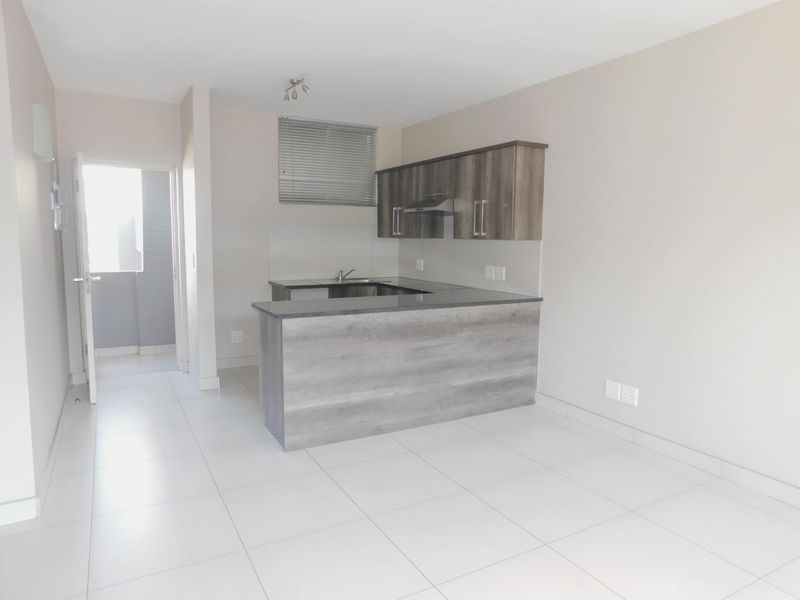 Open-plan kitchen featuring modern wood-finish cabinetry, granite countertops, and tiled flooring, leading to an adjacent living area.