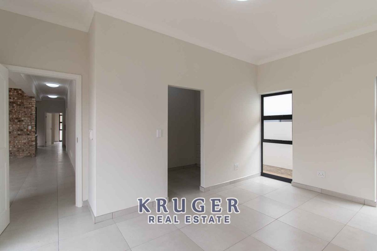 A bright, neutral-toned bedroom featuring tiled flooring, modern black-framed windows, and a walk-in closet area, leading into a tiled hallway.