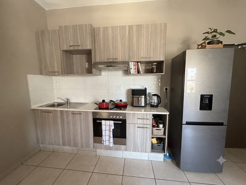 A functional kitchen featuring light wood-grain cabinetry, a built-in oven with electric hob, extractor fan, and tiled backsplash.