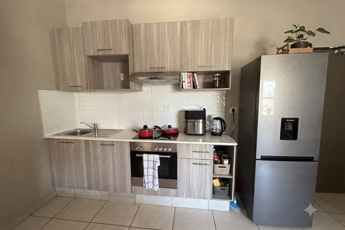 A functional kitchen featuring light wood-grain cabinetry, a built-in oven with electric hob, extractor fan, and tiled backsplash.