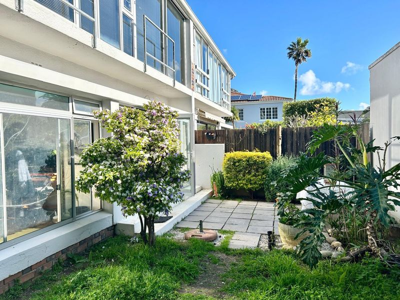Rear exterior view of the apartment featuring a paved patio area, sliding glass doors, and a private garden space with timber fencing.