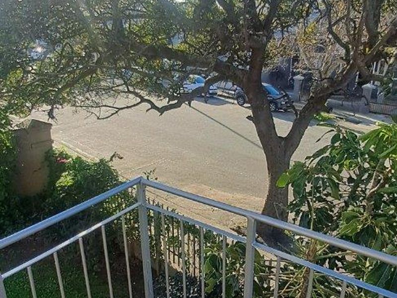An elevated balcony featuring a metal balustrade and tiled flooring, overlooking a street with mature trees.