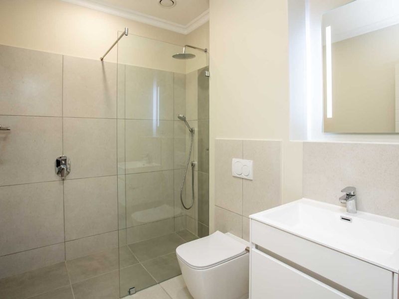 Modern bathroom featuring a walk-in shower with glass screen, wall-mounted toilet, and a sleek vanity basin with an illuminated mirror.