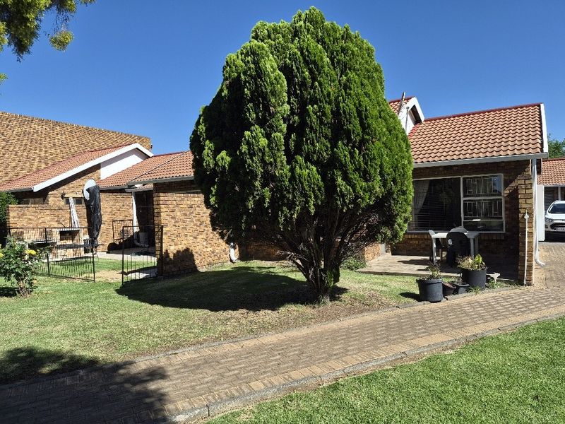 A view of the rear exterior of the apartment, featuring a brick facade, tiled roof, paved walkway, and a well-maintained garden area.