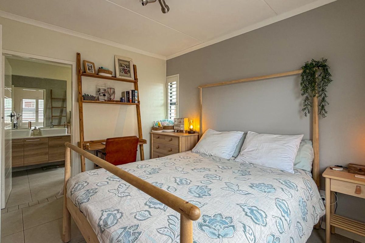 A well-maintained bedroom featuring neutral wall tones, tiled flooring, and an adjoining en-suite bathroom with a modern vanity.