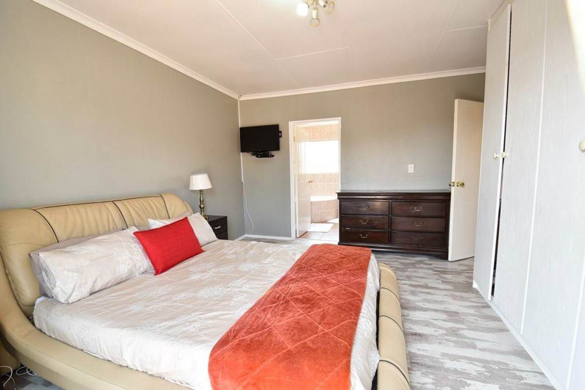 Spacious bedroom featuring built-in cupboards, light-toned wood-look flooring, and an en-suite bathroom access.