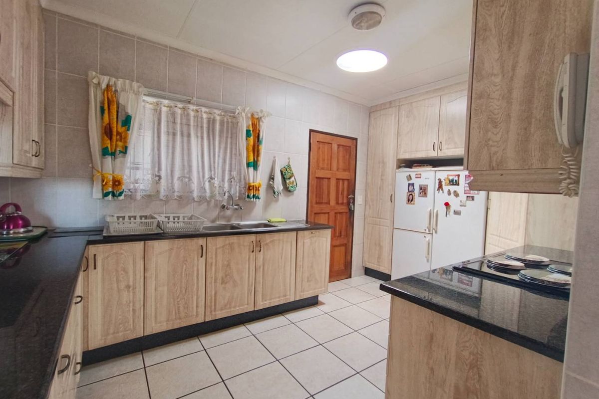 A functional kitchen featuring light wood-grain cabinetry, dark granite countertops, tiled flooring, and wall-mounted tiling, providing a practical and well-maintained workspace.
