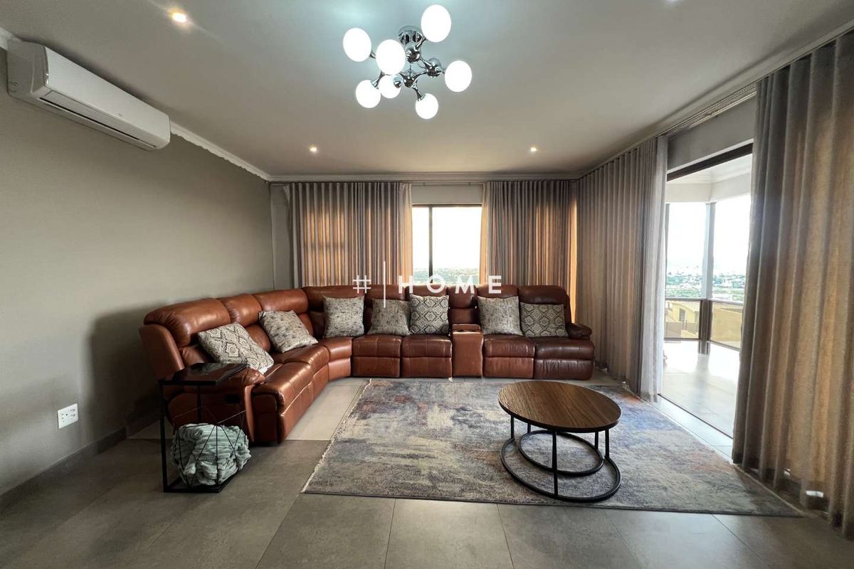 Spacious living room featuring large format floor tiles, recessed downlighting, a modern chandelier, and direct access to an outdoor balcony through sliding glass doors.