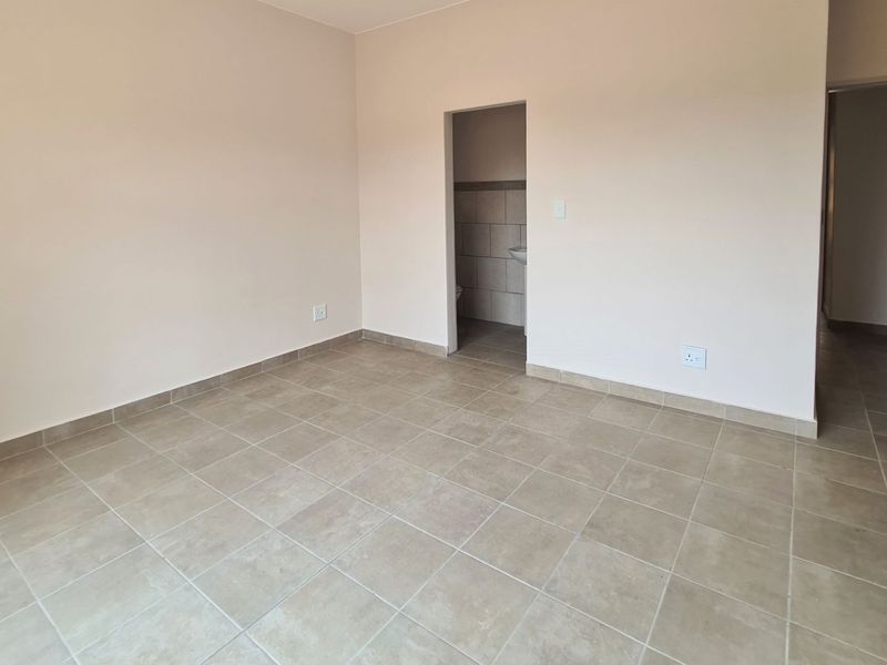 An empty bedroom featuring neutral tiled flooring, smooth walls, and access to an en-suite bathroom area.
