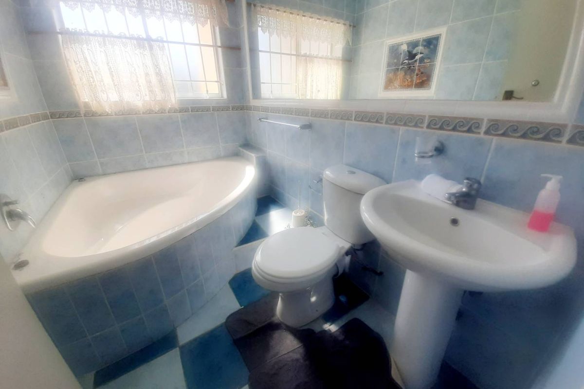 A dated bathroom featuring a corner bathtub, pedestal basin, and toilet with blue tiled walls and flooring.