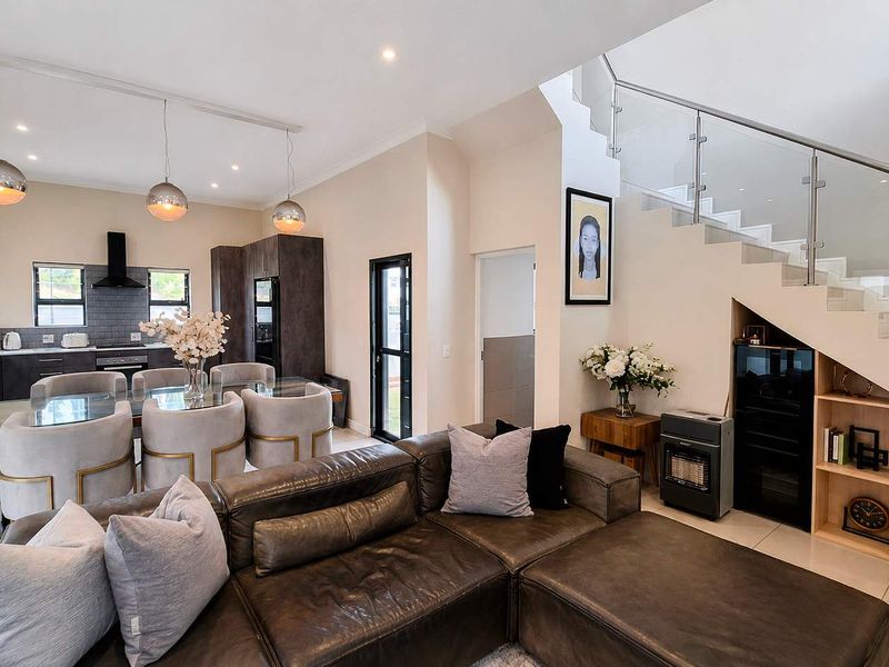 Modern open-plan living and dining area featuring a sleek kitchen, tiled floors, and a contemporary staircase with glass balustrades and integrated storage.