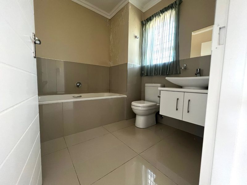 A compact bathroom featuring a built-in bathtub, wall-mounted vanity with basin, and toilet, requiring minor cosmetic repairs to the wall finish.