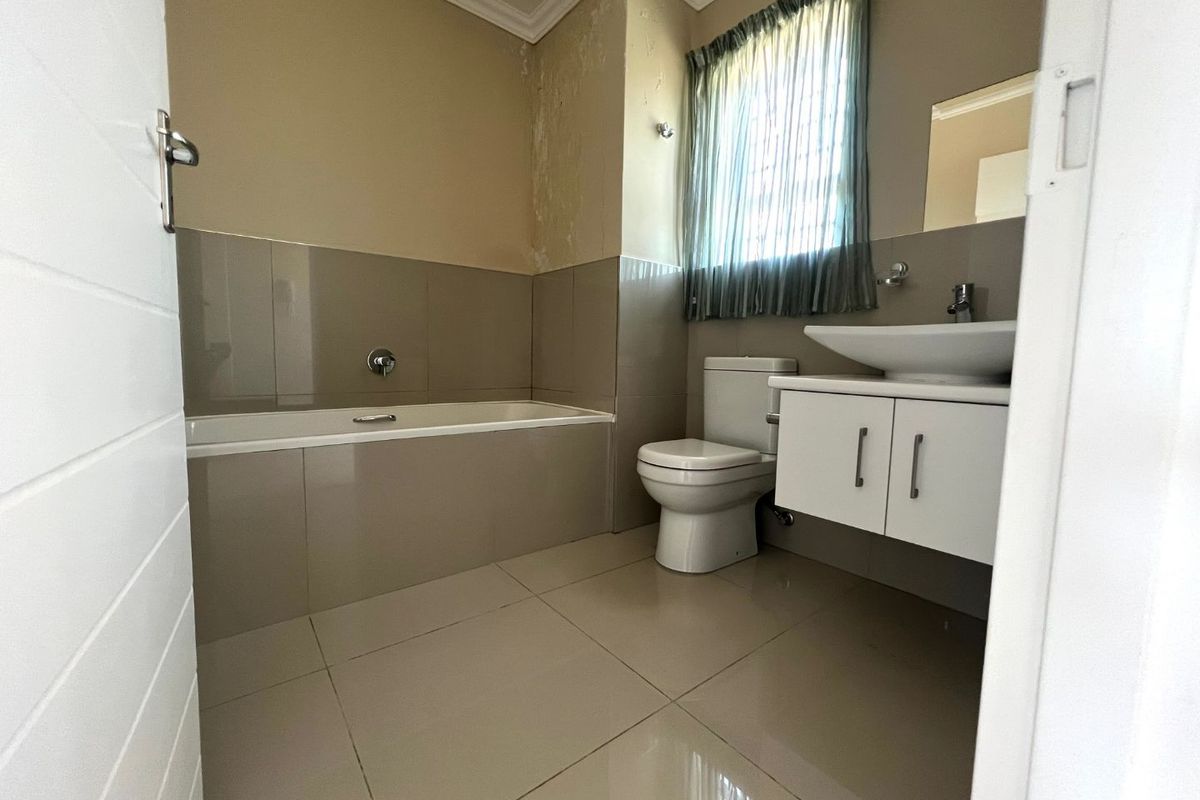 A compact bathroom featuring a built-in bathtub, wall-mounted vanity with basin, and toilet, requiring minor cosmetic repairs to the wall finish.