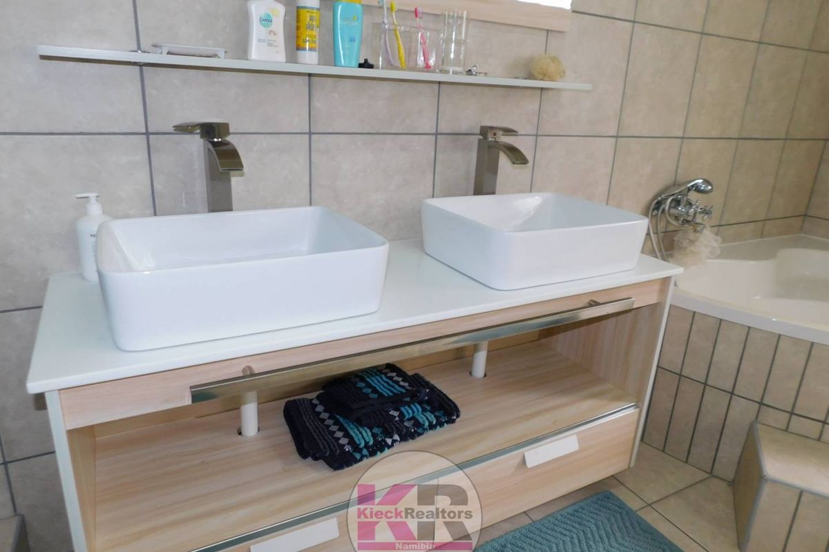 Modern bathroom featuring a double vanity with vessel sinks, contemporary faucets, and tiled wall finishes adjacent to a built-in bathtub.