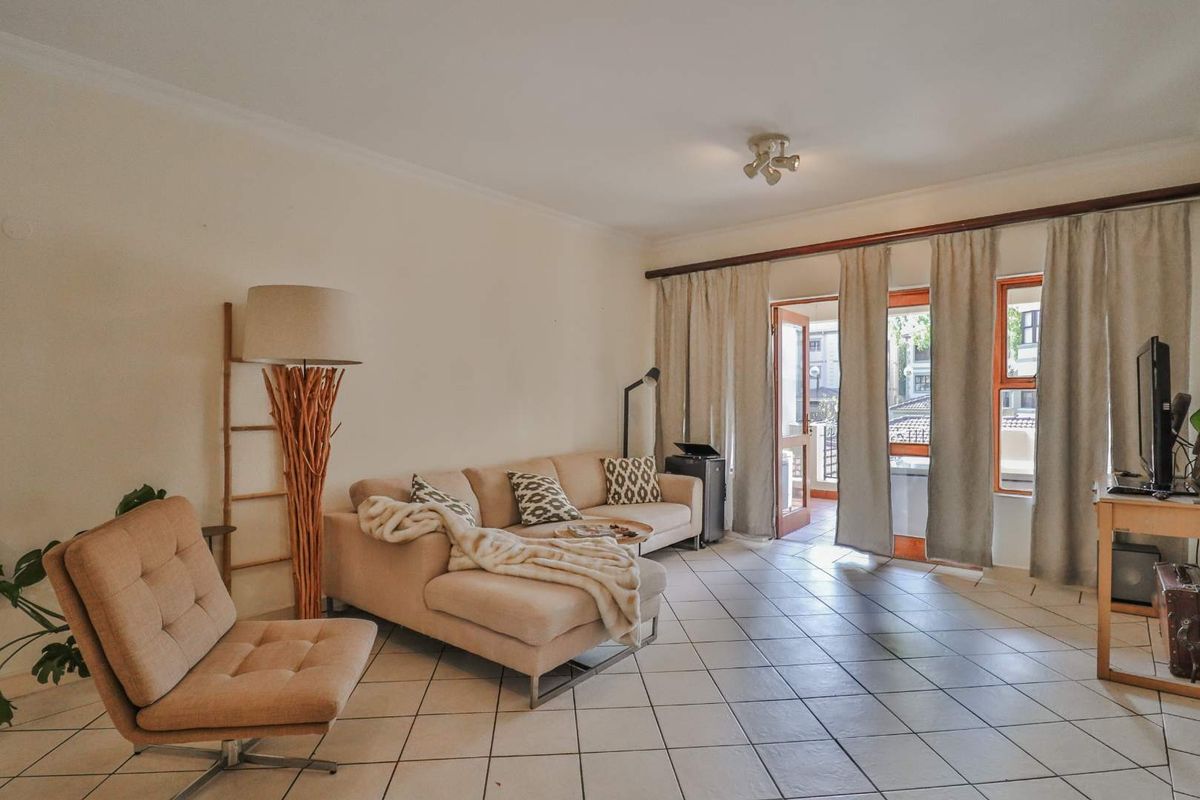 A bright living room featuring tiled flooring and direct access to an outdoor balcony through a glass-paneled door.