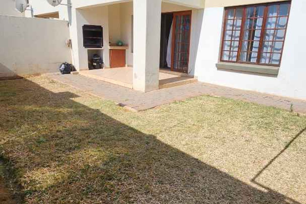 Rear view of the apartment featuring a private garden, paved patio area with a built-in braai, and balcony access.