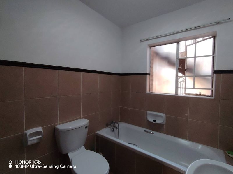 A dated bathroom featuring a standard bathtub, toilet, and brown ceramic wall tiles with a window providing natural light.