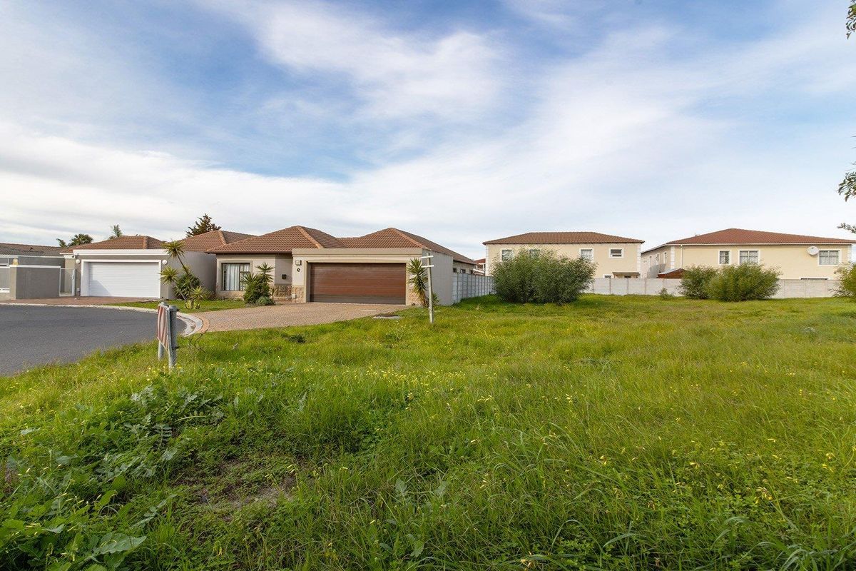 A vacant residential plot of land situated in a developed neighborhood, featuring a paved driveway access point and established boundary walls.