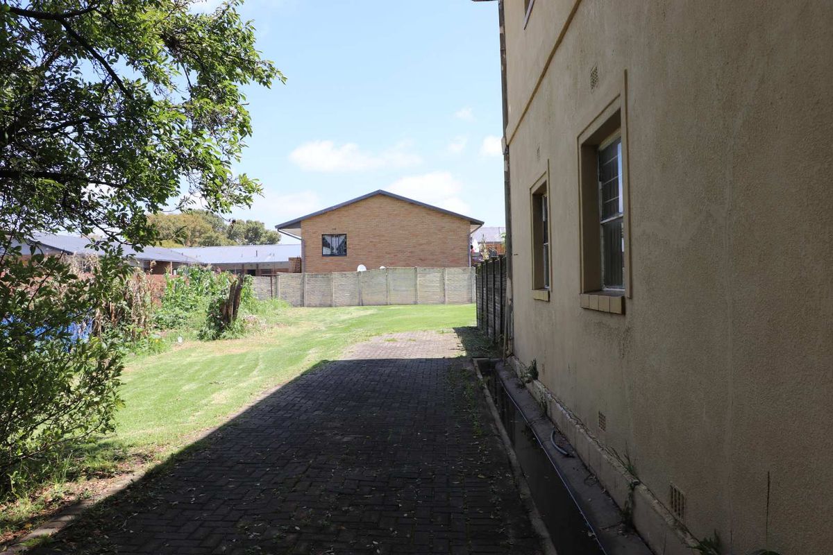 Side exterior view of the townhouse featuring a paved walkway, lawn area, and boundary walling.