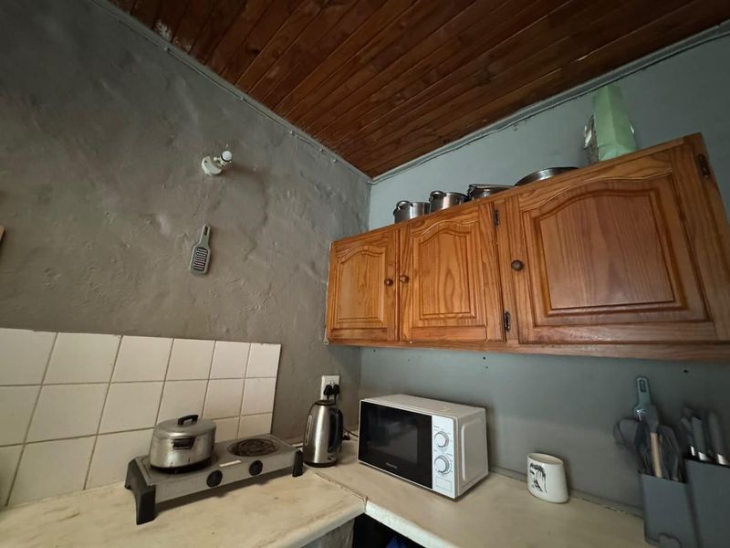 A compact kitchen area featuring wooden cabinetry, a tiled splashback, and a rustic wooden ceiling, requiring modernization of finishes and surfaces.