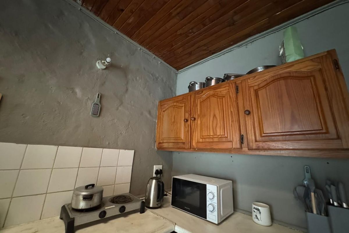 A compact kitchen area featuring wooden cabinetry, a tiled splashback, and a rustic wooden ceiling, requiring modernization of finishes and surfaces.