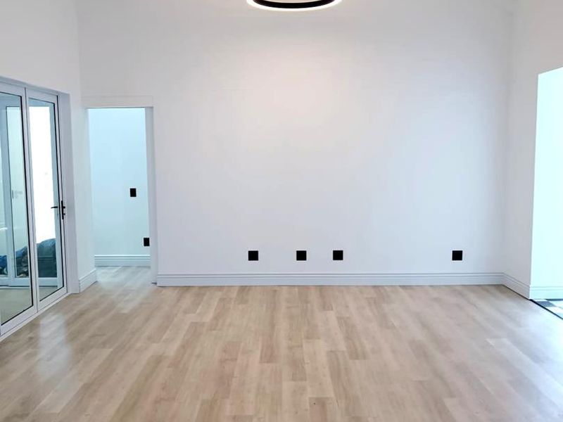 Spacious, light-filled living area featuring vaulted ceilings with exposed beams, modern pendant lighting, and high-quality laminate flooring with seamless access to outdoor areas.