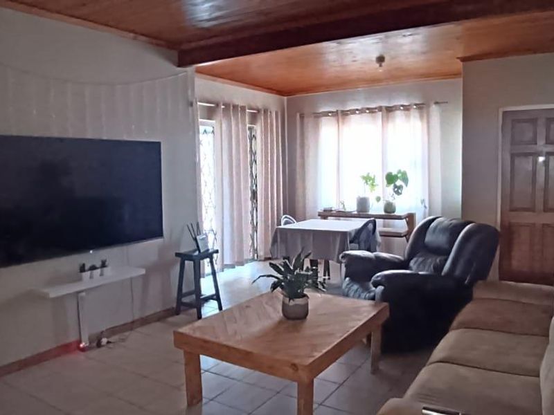 Spacious open-plan living and dining area featuring a warm timber-clad ceiling and tiled flooring, providing a comfortable and functional layout.