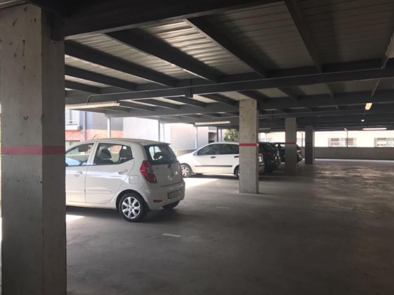 A covered parking garage area featuring concrete support columns and a metal roof structure, providing sheltered parking spaces.