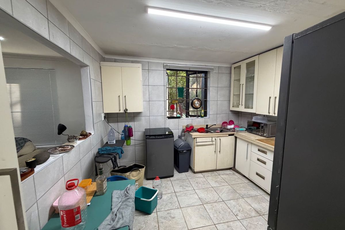 A functional kitchen space featuring tiled walls and floors, built-in cabinetry, and a stainless steel sink, offering potential for modernization and layout optimization.