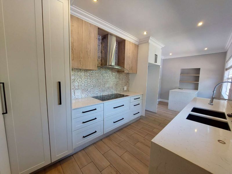 Modern kitchen featuring white and wood-tone cabinetry, quartz countertops, patterned tile backsplash, integrated hob, and high-quality finishes throughout.