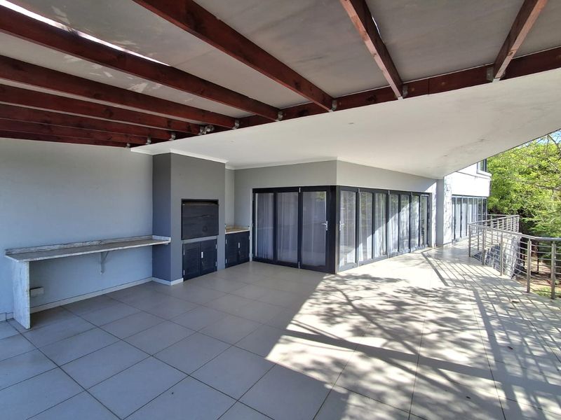 Spacious covered patio featuring a built-in braai, stone prep counter, and large folding glass doors, perfect for outdoor entertaining.