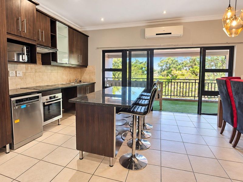 Modern open-plan kitchen and dining area featuring dark wood cabinetry, granite countertops, a central island, and direct access to a balcony.
