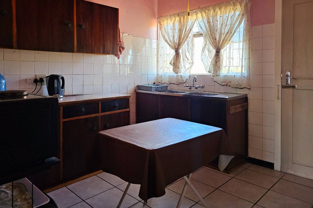A dated kitchen featuring dark wood cabinetry, tiled splashbacks, and a double basin sink with a window view.