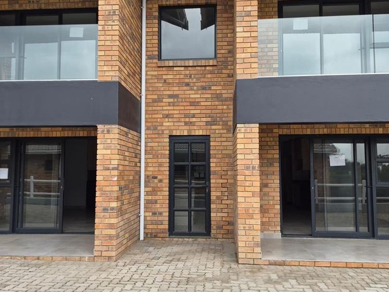 Modern townhouse exterior featuring face brick construction, glass balustrades on upper balconies, and paved driveway access to ground floor sliding doors.