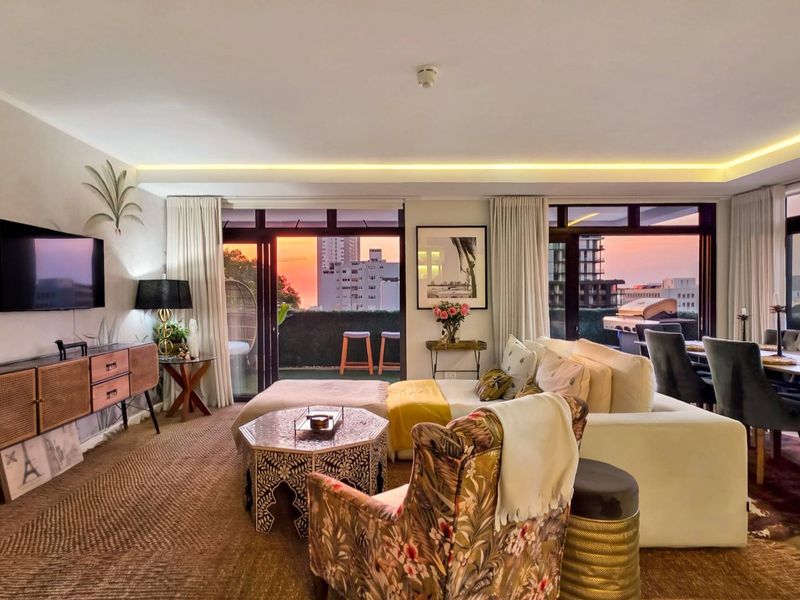 Spacious open-plan living area featuring recessed ceiling lighting and large sliding glass doors that open onto a private balcony with sunset views.