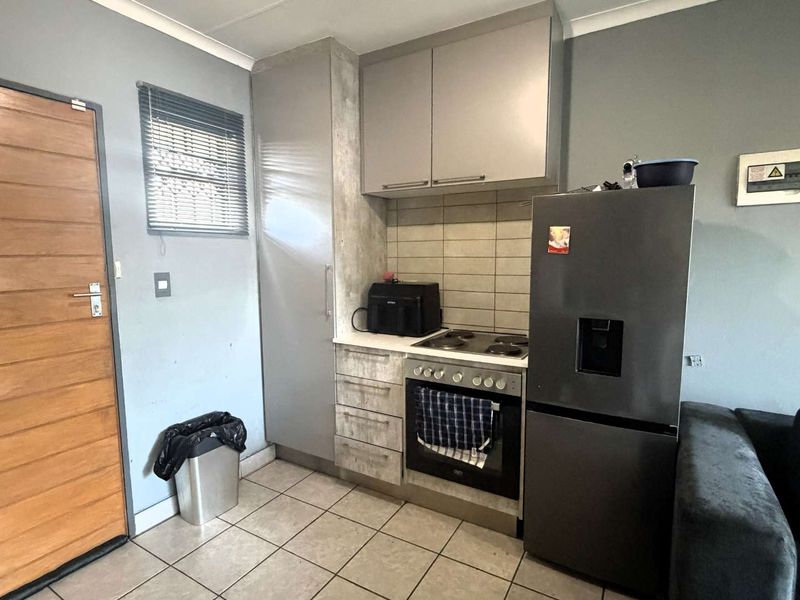 Compact open-plan kitchen area featuring built-in cabinetry, electric hob, oven, and tiled flooring, integrated within a living space.
