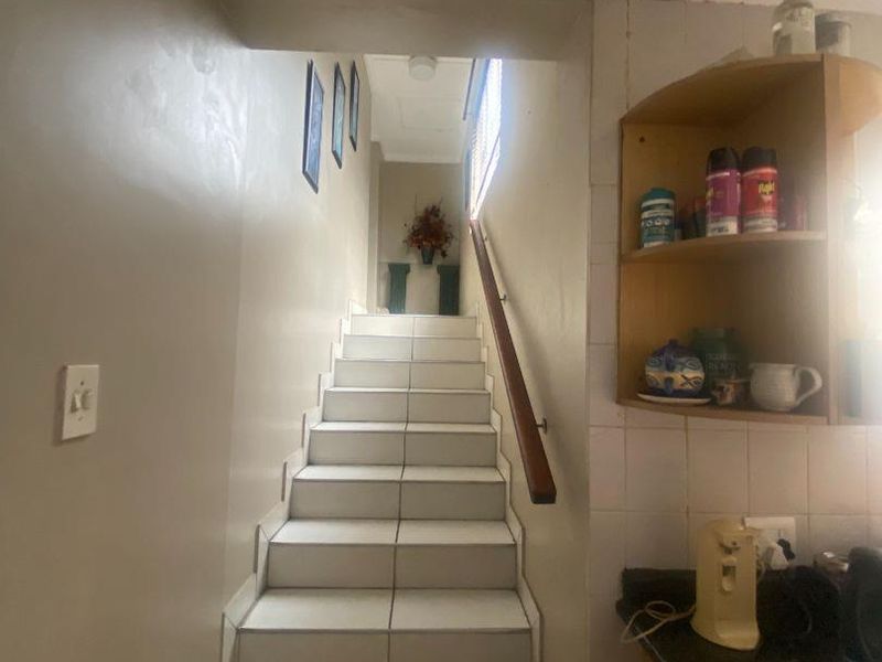 A staircase featuring tiled steps and a wooden handrail, leading to an upper level, adjacent to a kitchen area with built-in corner shelving.