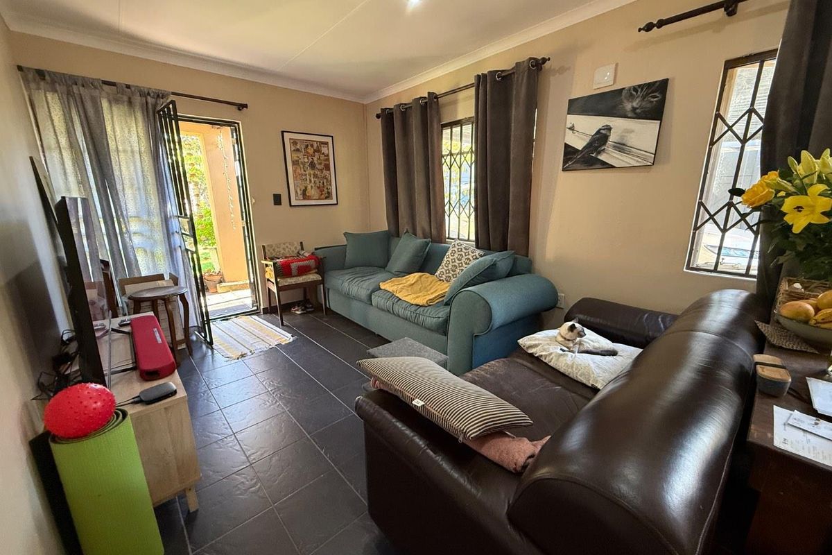 A comfortable living room featuring dark floor tiles, security gates on windows, and direct access to an outdoor patio area.