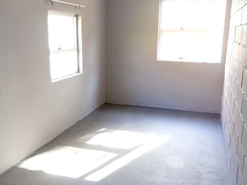 An empty bedroom featuring painted concrete flooring, exposed blockwork walls, and natural light from two windows.