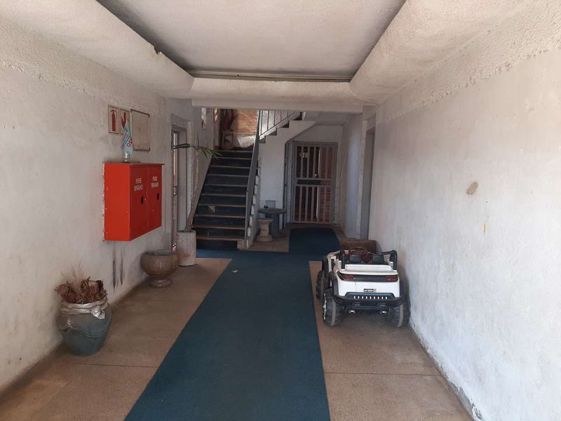 A communal apartment building hallway featuring a staircase, fire safety equipment, and a security gate, showing signs of wear and tear.